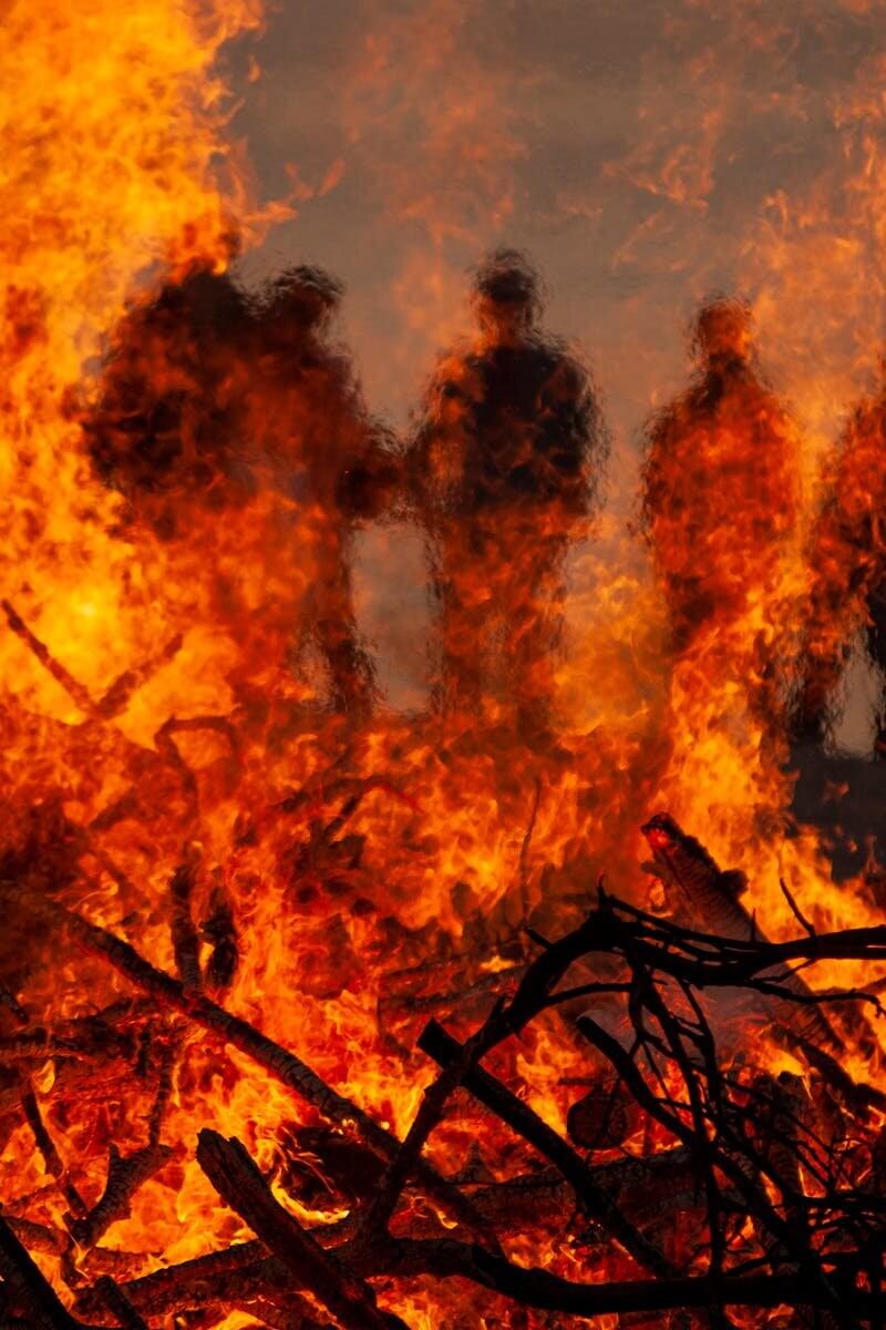 Dynamic silhouette of figures standing behind a large, blazing fire at night.