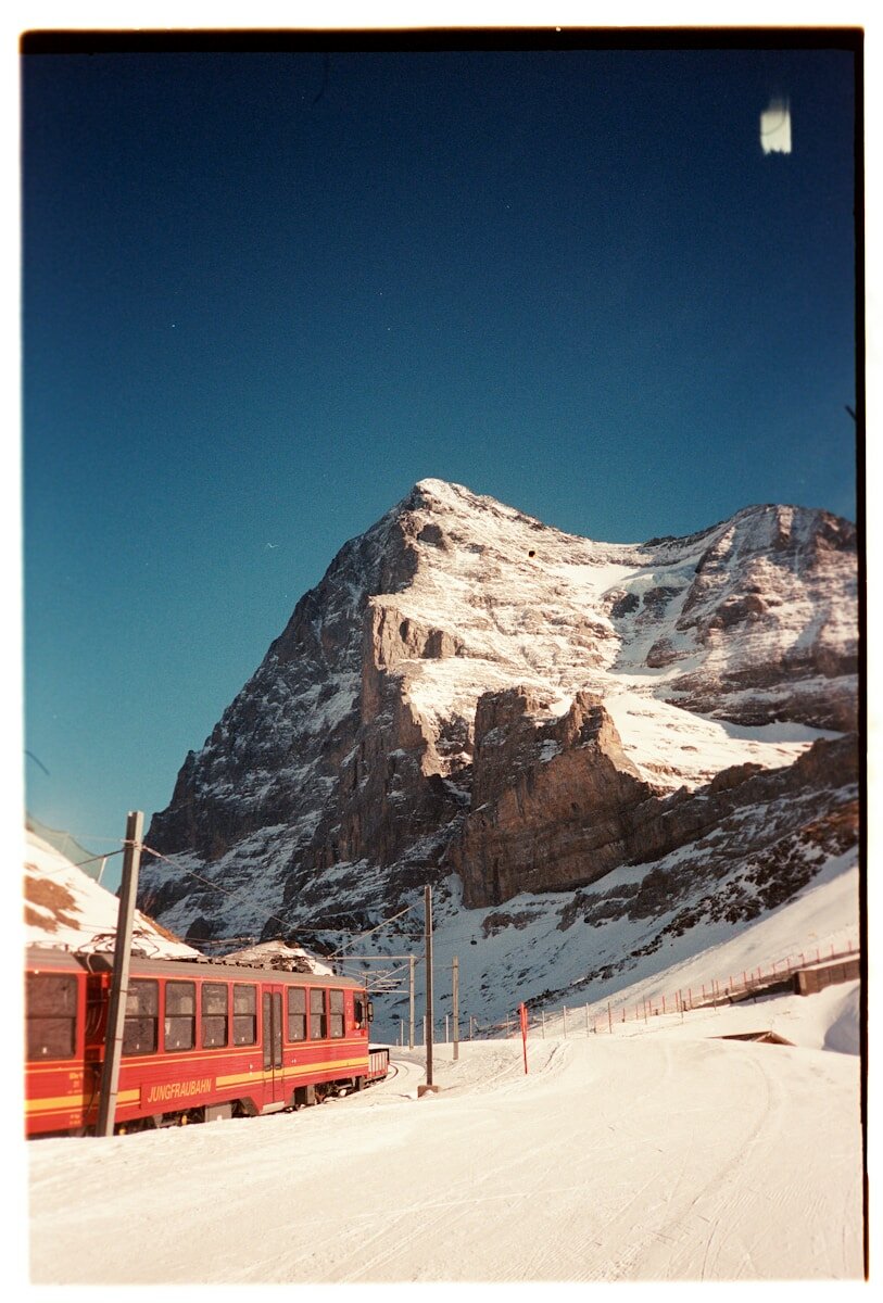 A red train travels through a snowy mountain landscape.