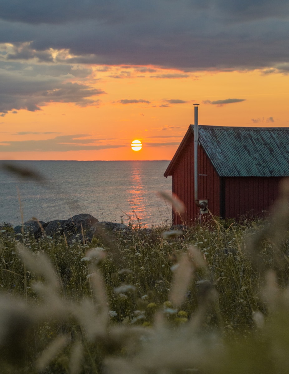 brown wooden house near body of water during sunset