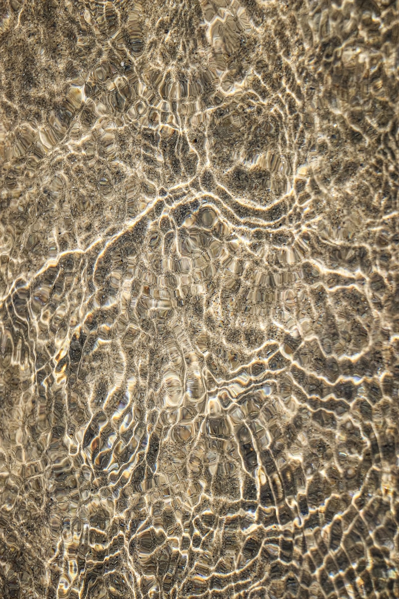 Rippling water creating light patterns on a sandy surface.