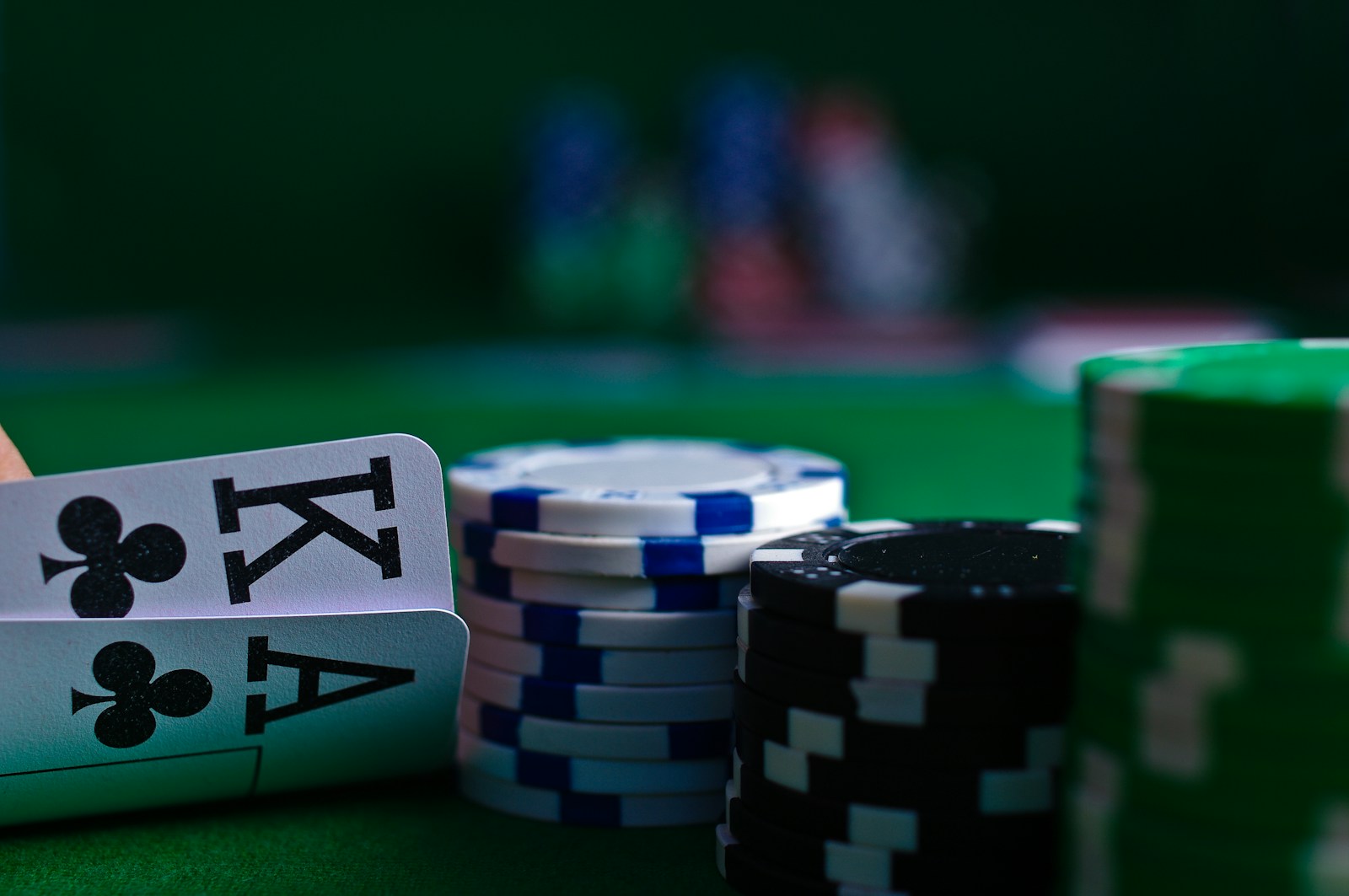 KINDERSPIELWOCHE - CASINOS 1 A hand holding playing cards beside stacks of poker chips on a green table