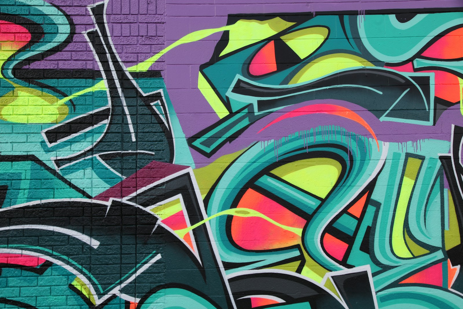 Ferienpass Grenchen - Wie sind Graffitis entstanden? 1 Vibrant graffiti with teal, purple, and neon yellow shapes on a brick wall