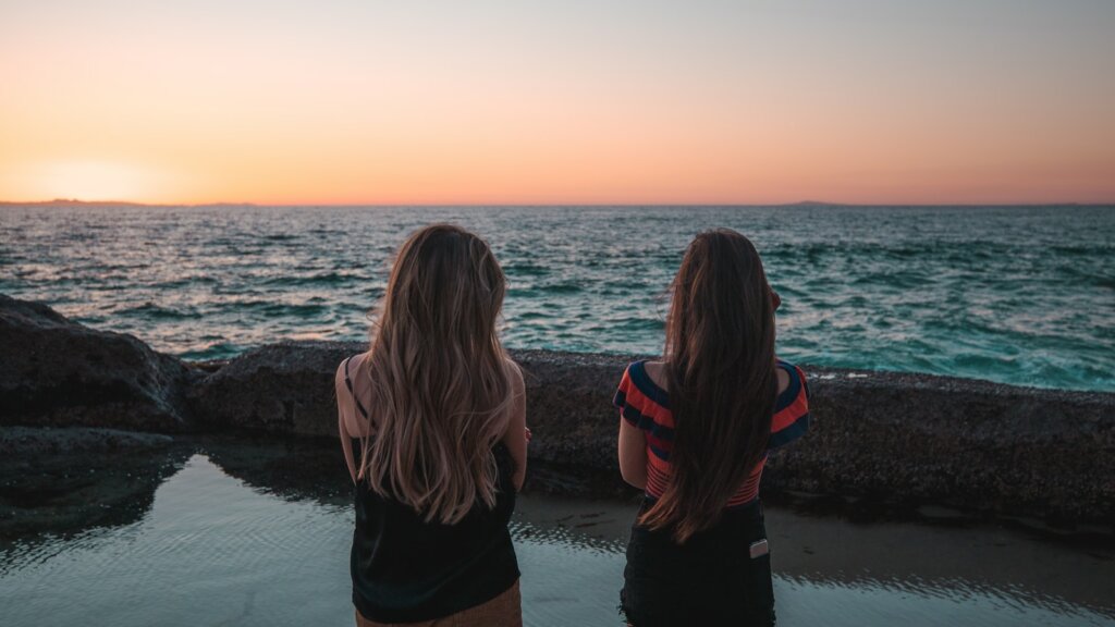 two woman standing facing body of water during daytime